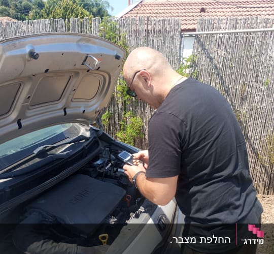 אדם בודק מנוע רכב עם מכשיר אלקטרוני